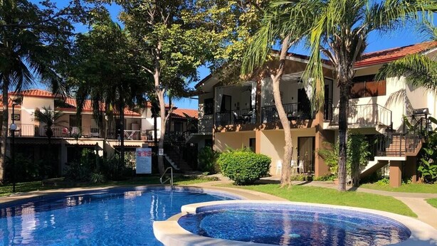 Ein Swimmingpool mit Whirlpool, umgeben von Palmen und einem Gebäude mit Balkonen.