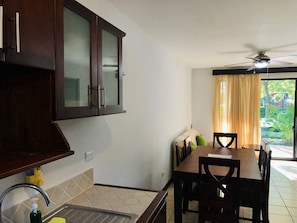 A kitchen with dark wooden cabinets, a dining area with a table and chairs, and a view of greenery outside.