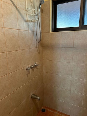 A small shower room with tiled walls, a window, and a showerhead.