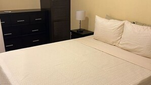 Un lit avec un matelas matelassé, une table de chevet avec une lampe, une armoire de couleur sombre et un grand miroir rond fixé au mur.