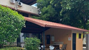Un espace aménagé au bord de la piscine, comprenant un coin salon couvert, une piscine et un bâtiment équipé de climatiseurs.