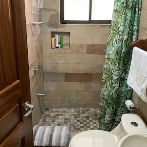 A bathroom with a shower, toilet, and a small shelf with toiletries.