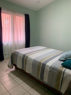 A bedroom with a bed, curtains, and a window.
