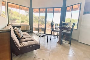 A modern living room with a sofa, a small table, and a dining area with chairs.