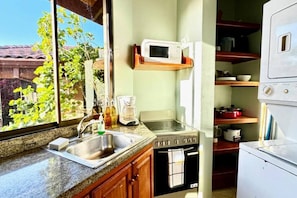 A compact kitchen with a sink, stove, microwave, and a window with a view of greenery.
