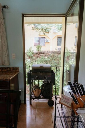 Eine Küche mit Grill, ein Essbereich mit Tisch und Stühlen sowie ein Blick auf ein Gebäude durch eine Glastür.