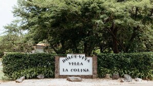A sign for 'Dolce Vita Villa La Colina' with a stone base, surrounded by greenery and trees. - Dolce Vita La Colina in Ocotal (Ocotal)
