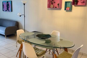 Un comedor moderno con una mesa de vidrio, sillas blancas y un sofá gris al fondo.