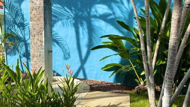 A pool area with a stone pillar, tropical plants, and a blue sky. - Villa Riviera Walk to Beach Condo Playas del Coco (Del Coco Beach)