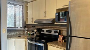 A compact kitchen with a stove, oven, refrigerator, and a window with blinds. - Villa Riviera Walk to Beach Condo Playas del Coco (Del Coco Beach)