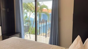 A hotel room with a bed, a chair, and a balcony with a view of palm trees and a building. - Villa Riviera Walk to Beach Condo Playas del Coco (Del Coco Beach)