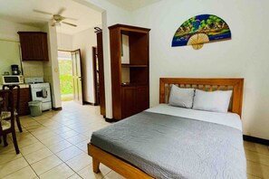 A bedroom with a bed, a wooden headboard, a wall-mounted artwork, and a kitchen area with cabinets and appliances. - Dreamed Vacations at Little Dreams (Ocotal)