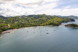 Una zona costiera con barche, una spiaggia e un pendio collinare ricoperto da una fitta vegetazione.