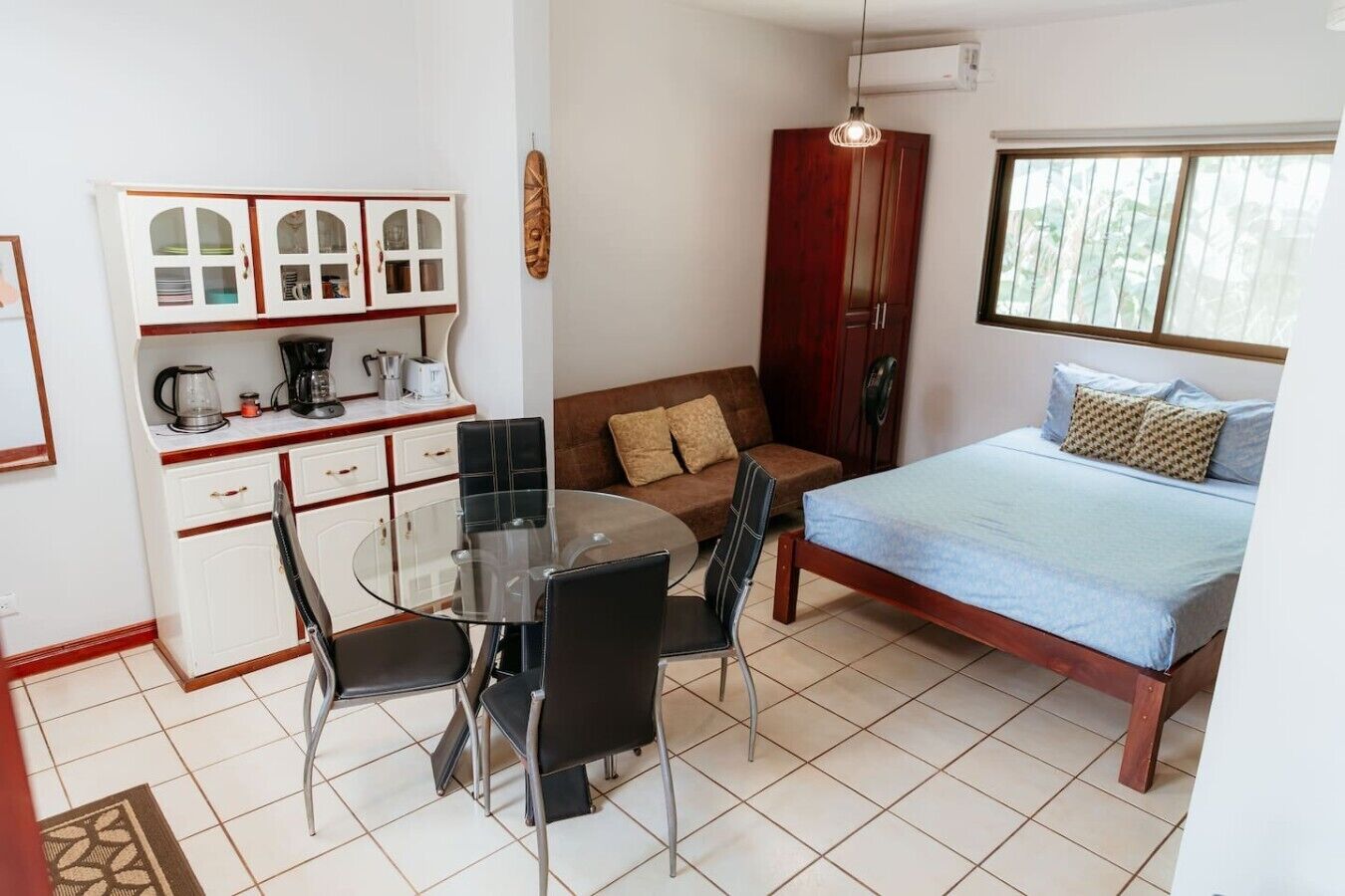 Una habitación compacta con cama, sofá, mesa de comedor con sillas, kitchenette y ventana.