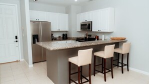 A kitchen with white cabinets, a stainless steel refrigerator, a microwave, and a granite countertop island with bar stools. - Lovely 2 bdrm Condo in Pacifico (Coco)