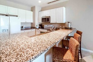 A kitchen with white cabinets, a granite countertop, a microwave, an oven, and a coffee maker.
