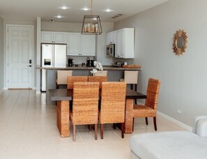 A modern kitchen with white cabinets, a dining area with wicker chairs, and a white sofa. - Lovely 2 bdrm Condo in Pacifico (Coco)