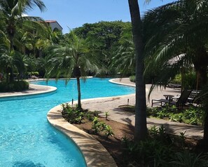Ein Pool mit geschwungener Kante, umgeben von Palmen und Liegestühlen.