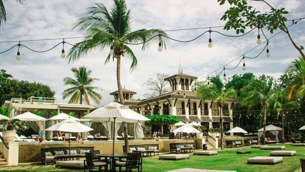 A resort with outdoor seating, palm trees, and string lights. - Lovely 2 bdrm Condo in Pacifico (Coco)