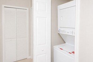 Ein Waschraum mit nebeneinander stehender Waschmaschine und Trockner, einer weißen Tür und einem Schrank mit Klappläden.