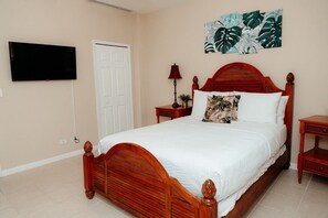 A bedroom with a wooden bed, a flat-screen TV mounted on the wall, a door, and a wall-mounted artwork.