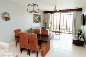 A modern living room with a dining area, large windows, and a ceiling fan. - Lovely 2 bdrm Condo in Pacifico (Coco)