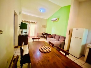 A dining area with a wooden table, chairs, a sofa, a television, and a refrigerator.