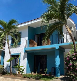 A two-story building with a blue and white exterior, a balcony, and palm trees.