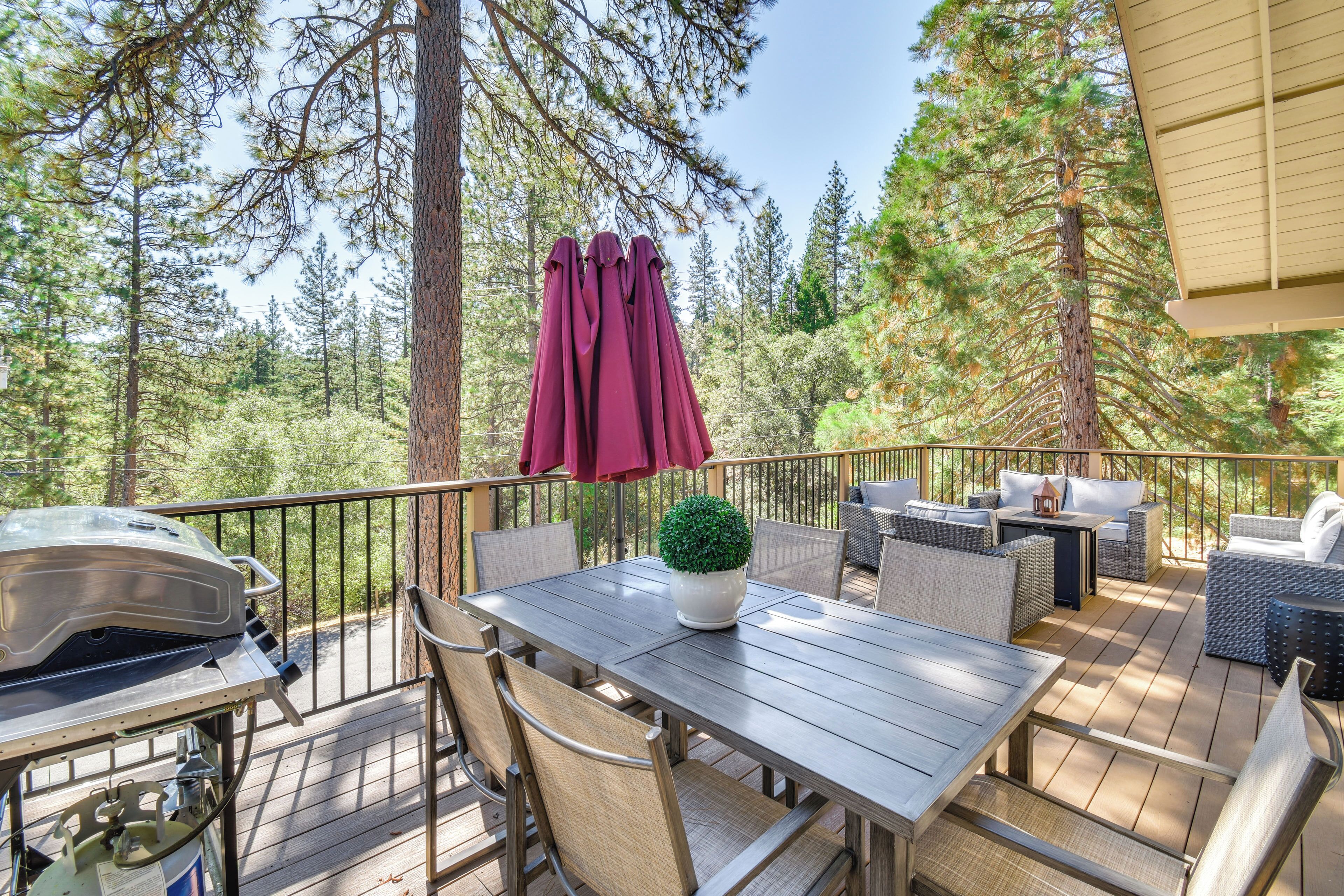 Une terrasse en bois, dotée de mobilier d’extérieur, d’un barbecue et offrant une vue sur une forêt.