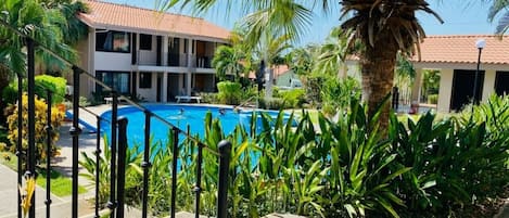 Zona de piscina con una piscina azul cristalina, rodeada de exuberante vegetación y una palmera.