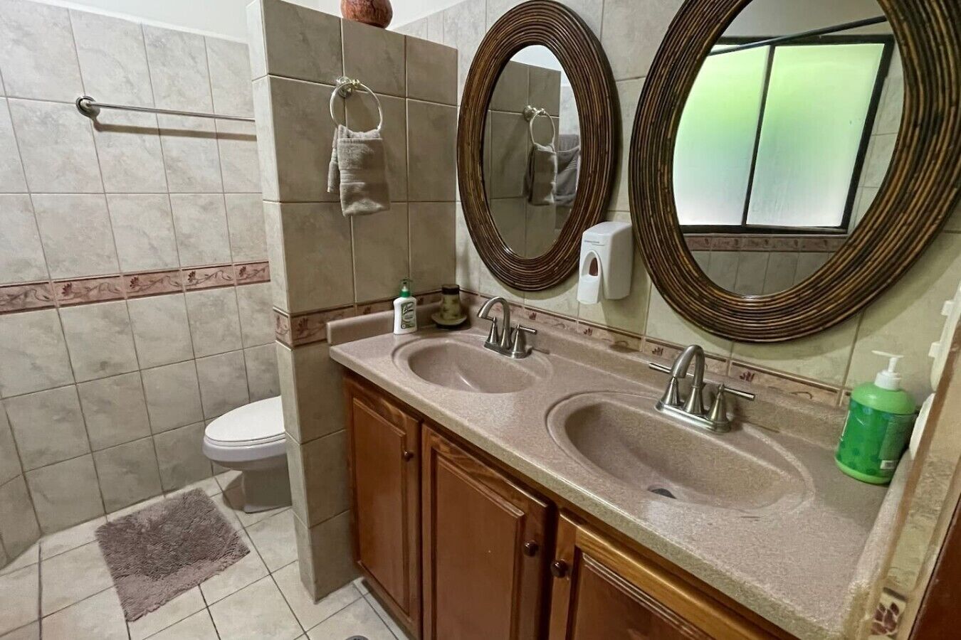 Un baño con dos lavamanos, un inodoro, un perchero para toallas y dos espejos.