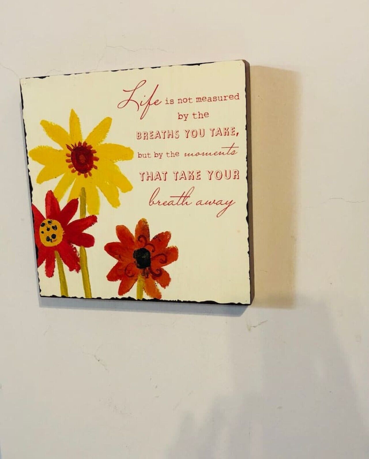 Une carte décorative à accrocher au mur, ornée d’une citation sur la vie et le souffle, et accompagnée de trois fleurs stylisées.