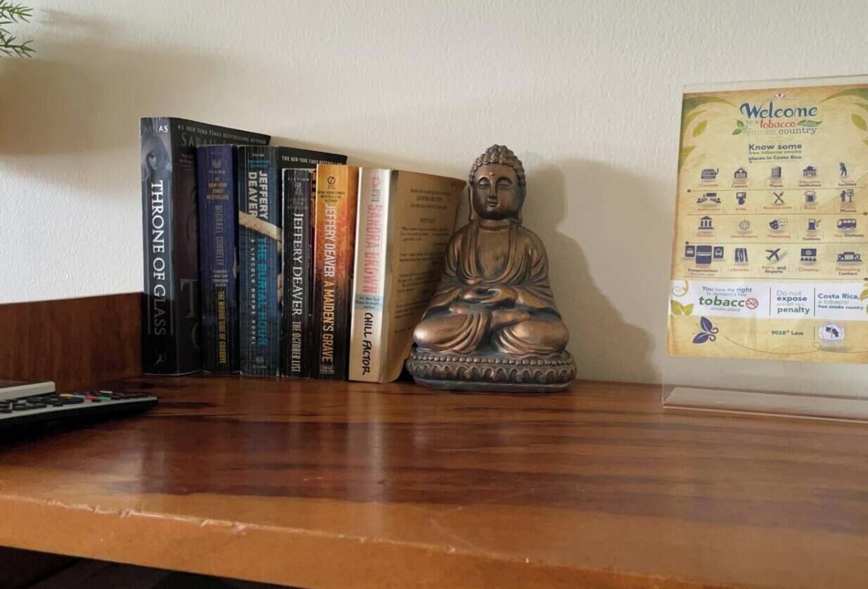 Uno scaffale in legno con libri, una statua di Buddha e un cartello di benvenuto.