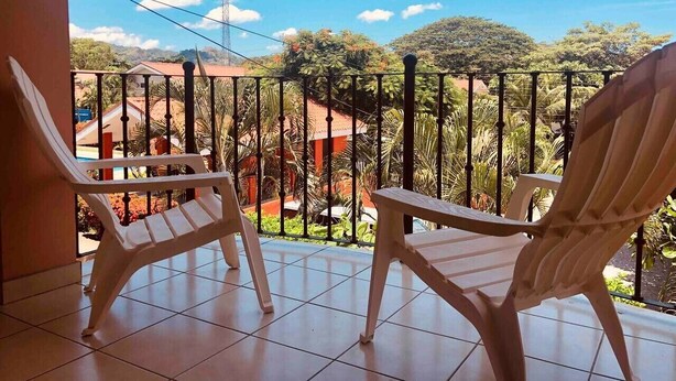 Ein Balkon mit zwei weißen Kunststoffstühlen, gefliestem Boden und Blick auf eine Wohngegend mit Häusern und Grünflächen.