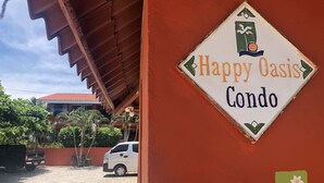 Schild für Happy Oasis Condo mit einer roten Wand und einem weißen Auto im Hintergrund.