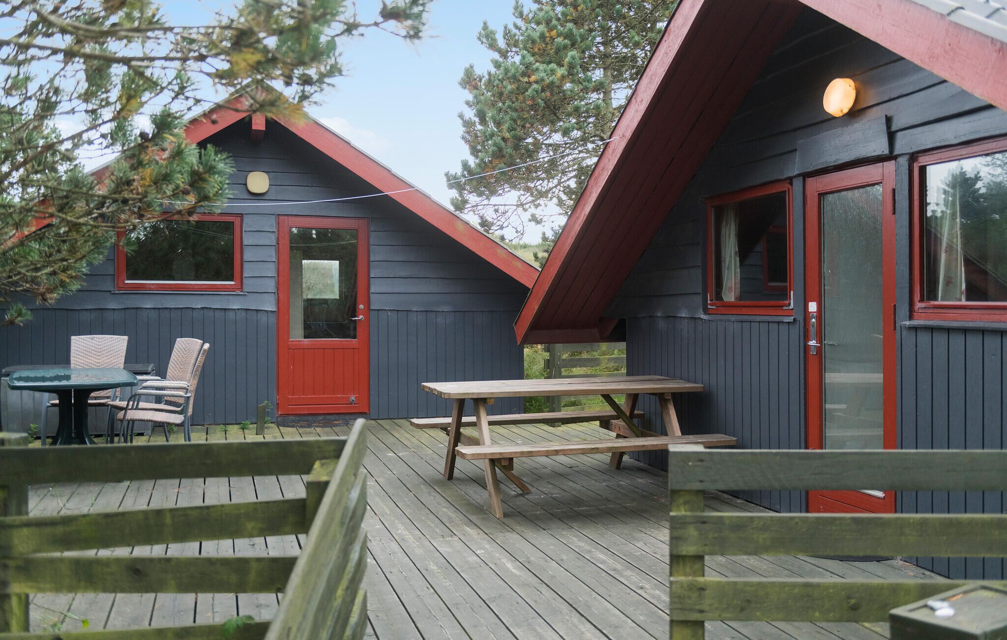 A cabin with a red door and windows, a wooden deck, and a picnic table.