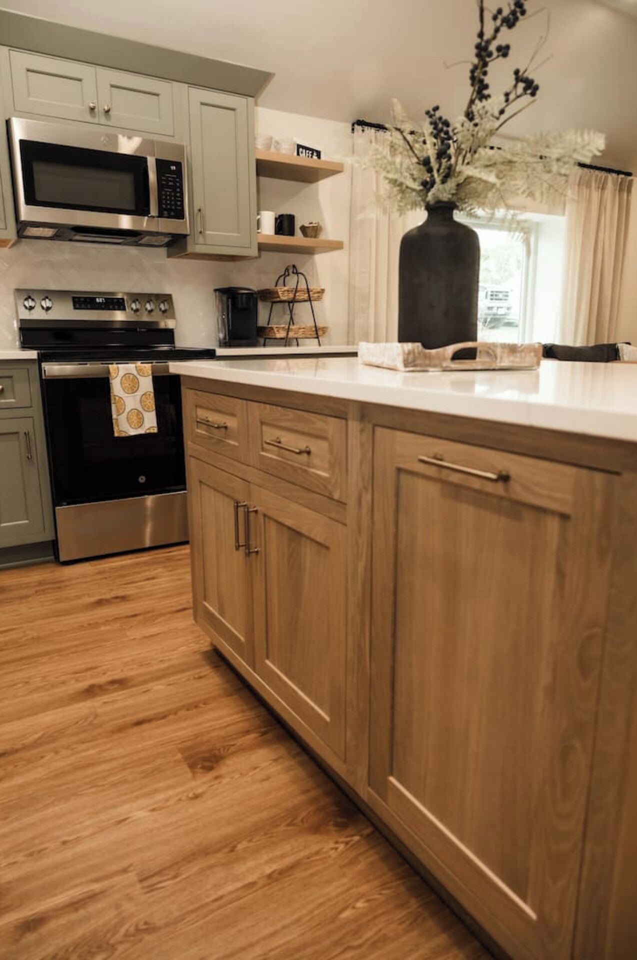 Une cuisine avec des meubles de couleur bois clair, des appareils électroménagers en acier inoxydable et un plancher en bois.