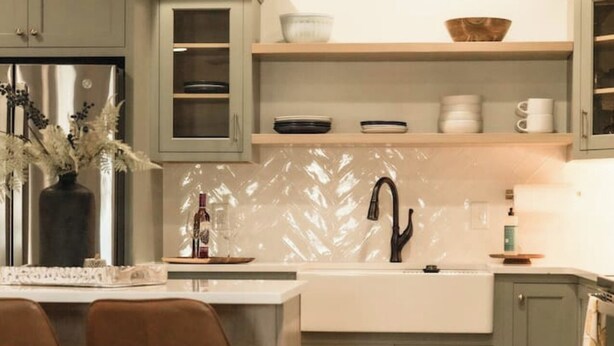 Een moderne keuken met grijze kastjes, een centraal eiland en een eethoek met bruine stoelen.