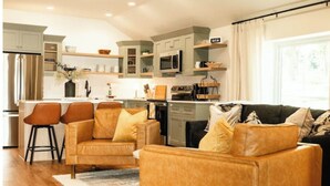Een moderne keuken met een centraal eiland, een zithoek met twee stoelen, en een woonkamer met een bank en salontafel.