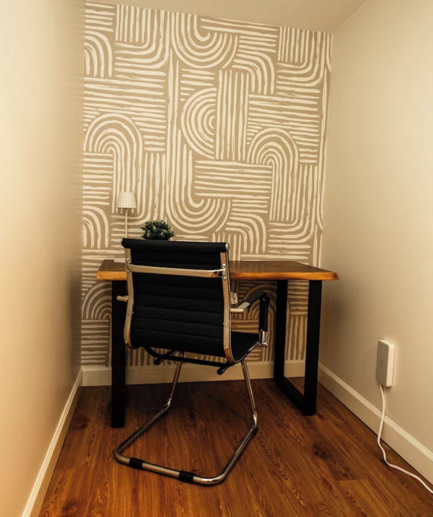 A corner room with a wooden desk, a black office chair, and a patterned wallpaper.