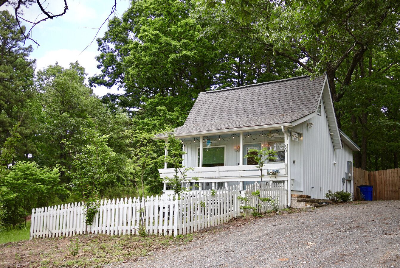 A white house with a porch, surrounded by a white picket fence and trees.
