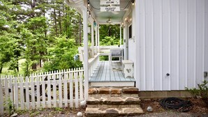 A white cottage with a porch, stone steps, and a white picket fence.