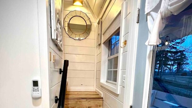 A wooden staircase leading to a door with a window, white walls, and a small mirror on the wall.