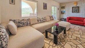 A living room with a beige sectional sofa, a red couch, a glass coffee table, and a patterned rug.