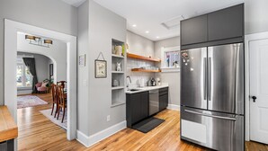 A modern kitchen with a stainless steel refrigerator, wooden flooring, and built-in shelves. - Cozy Victorian | King Bed, Private Yard, Walk to SoBo Restaurants (Denver)