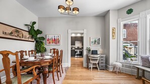 A dining area with a wooden table and chairs, a kitchen in the background, and a view of the outside through a window. - Cozy Victorian | King Bed, Private Yard, Walk to SoBo Restaurants (Denver)