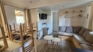Ein modernes Wohnzimmer mit einer Couch, einem Esstisch mit Stühlen, einem an der Wand befestigten Fernseher und einem kleinen Regal mit Dekoration.