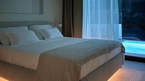 A modern hotel room with a large bed, a bedside table, and a view of a pool. - Luxurious home in Zman (Zman)