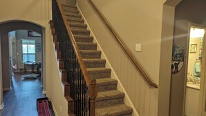 Un intérieur de maison à plusieurs niveaux, avec un escalier recouvert de moquette, des rampes en bois et un couloir menant à une salle à manger.