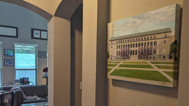 Un salon avec un canapé, une table basse et un tableau représentant un bâtiment accroché au mur.